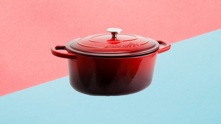 Crock Pot Artisan Sieben-Quart Ovaler Dutch Oven aus emailliertem Gusseisen in Rot vor rosa und blauem Hintergrund.