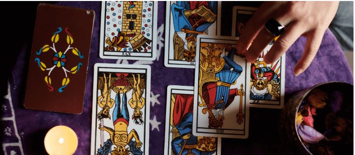 Ein Mensch legt kunstvoll gestaltete Tarot-Karten auf einem Tisch aus, um das Jahr 2023 vorzubereiten.
